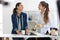 Two pretty young businesswomen drinking coffee while taking a break in a sewing workshop