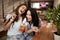 Two pretty youthful smiling girls,dressed in casual outfit,sit next to each other and look at the camera in a cozy