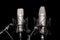 Two professional silver studio microphones on stands on black background, podcasting, voiceover. Interview or sports event