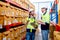 Two professional warehouse worker men discuss about work and stay between shelves with product in workplace and they look happy