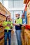 Two professional warehouse workers stand between shelves of products and discuss together about work in workplace area. The