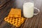 Two puff cookies, transparent cup with milk on wooden table