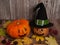 Two pumpkins with funny painted faces, a magic witch hat, cones and colorful autumn leaves on a wooden background.