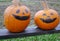 Two pumpkins painted as halloween face, placed on wooden table at a farm.