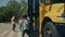 Two pupils leaving schoolbus chatting. Teenagers standing talking near bus.