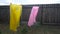 Two raincoats pink and yellow flutter from the wind in the courtyard of the house against the background of the fence.