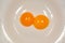 Two raw chicken yolks in a white plate, separate from the eggs.