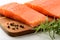 Two raw chilled salmon fillets, pepper grains and fresh rosemary on a brown wood cutting board. Healthy eating, seafood recipe