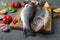 Two raw fish seabass with ingredients and seasonings like basil, lemon, salt, pepper, cherry tomatoes and garlic on