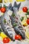 Two raw fresh sea bass ready for baking with tomatoes, lemon, red onion, garlic, ginger, parsley and spices. Prepare a tasty and