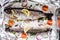 Two raw river trouts with thyme, lemon, red onion and tomatoes in foil closeup