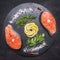 Two raw salmon steak on a stone cutting board with salt, pepper, herbs , lemon, lined all around, top view