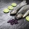 Two ready to cook raw river trouts with herbs on stone black textured background.