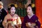 Two real geisha meiko and geiko hosting an event at Yasaka Shrine, wearing colorful kimono and traditional white make-up.