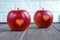Two red apples with a heart seal on the table. Orange heart on organically grown fruits. Growing fruits with prints