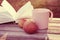 Two red apples, pink mug and open book on wooden bench in rays of sunlight