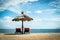 Two red beach chairs under wicker umbrella on a coast.