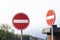 Two red circular traffic signs or roadsign with a white bar indicating no entry on a grey metal post against a cloudy sky in a