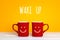 Two red coffee mugs with a smiling faces on a yellow background