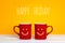 Two red coffee mugs with a smiling faces on a yellow background