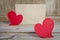 Two red fabric hearts on a wooden board