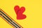 two red felt hearts and two bracelets with lgbt colors on yellow background copy space top view, pride concept