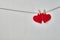 Two red felt valentine hearts hanging from a rope on white wooden background