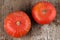 Two red kuri squashes on a rough woody texture background.