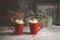 Two red mugs with hot chocolate, whipped cream, Christmas star cookie and cinnamon sticks standing on table with snow and gifts