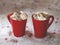 Two red mugs with hot chocolate and whipped cream on table with snow. Cozy warm drinks at home with sweet cream. Front view