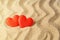 Two red silk hearts on a yellow wavy sea sand. Concept of love, sun, hot summer, sea holiday and vacation on a beach