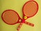 Two red small plastic tennis rackets on yellow paper