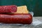 Two red sticks of salami sausage and a piece of cheese on a gray wooden table