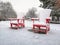 Two red wooden Adirondack Muskoka chairs covered with snow on winter day in park outdoors. Winter season Canadian landscape in