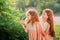 Two redhead sisters in long linen dresses are walking in park on sunny summer day