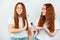 Two redheaded young women standing on isolated white backgroung, one wants to curl her friend`s hair with styler, but she refuses