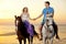 Two riders on horseback at sunset on the beach. Lovers ride horseback. Young beautiful man and woman with a horses at the sea.