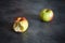 Two ripe apples, one bitten and one whole on a dark background.