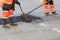 Two road builders assemble and level fresh asphalt with a whisk and level on the repaired part of the road