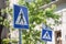 Two roadsigns warning drivers of the presence of a crosswalk with pedestrians crossing in an urban landscape