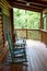 Two rocking chairs and a swing on a wooden wrap around deck