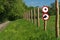 Two round red warning signs on a fence post in front of a green