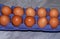 Two rows of brown raw uncooked fresh chicken eggs in purple carton tray