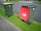 two rubbish containers with red and yellow lids on green grass