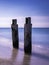 Two ruined pilings and white waves rolling in on blue sea background