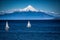 Two sailboats sail in front of snow capped Orsono Volcano in Chile