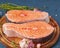 Two salmon steaks, fish fillet, large sliced portions  on chopping board on a dark table. Side view