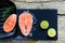 Two salmon steaks are ready to cook on a grill, along with lime on a wooden background. Top view. Healthy food