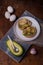 Two sandwiches with avocado, boiled eggs and red onions on white plate, avocado half on wooden background. Vertical shot