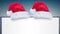 Two santa hats over a blank placard against snow falling on blue gradient background